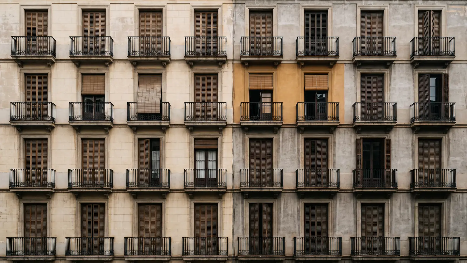 Vista frontal de una fachada del Eixample de Barcelona con una retícula de balcones idénticos repetidos en hileras, unos con las persianas bajadas, otros a medio subir y otros abiertos.
